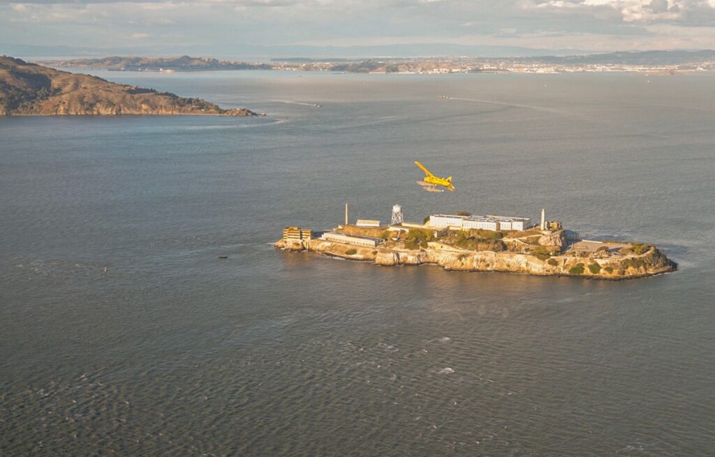 yellow seaplane flying above Alcatraz Prison Island