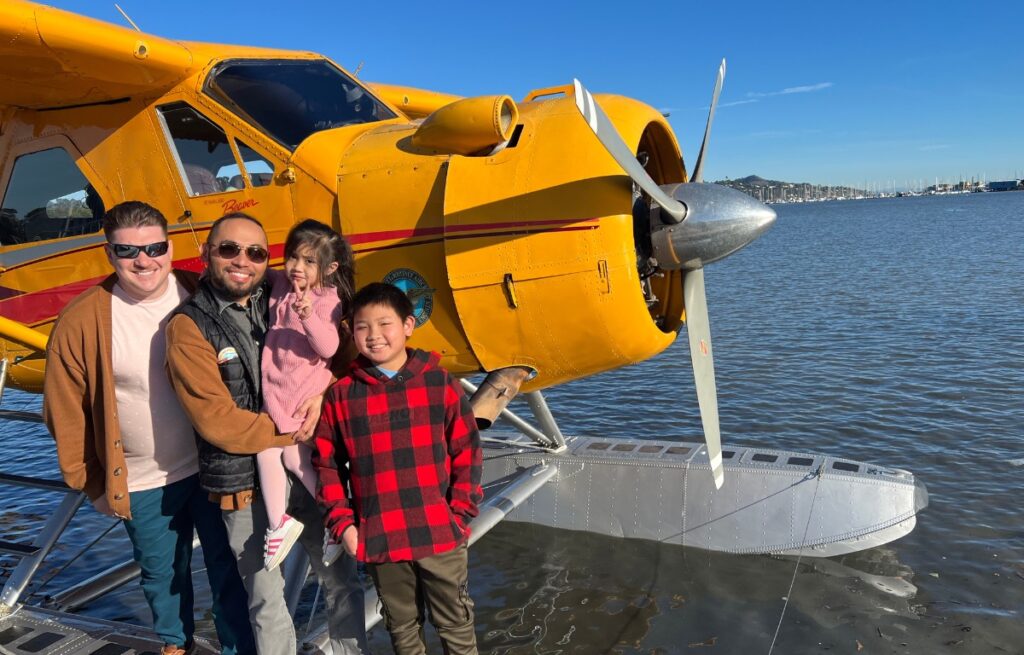 A family smiles on the dock in front of a yellow seaplane