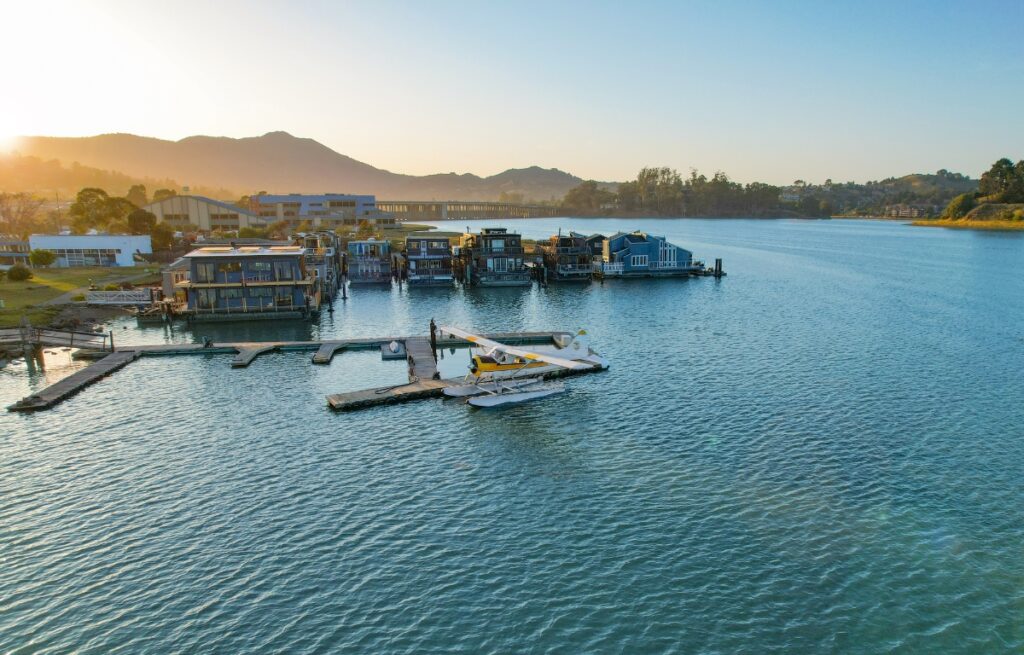 A yellow seaplane is shown docked on the water with a mountain skyline behind it